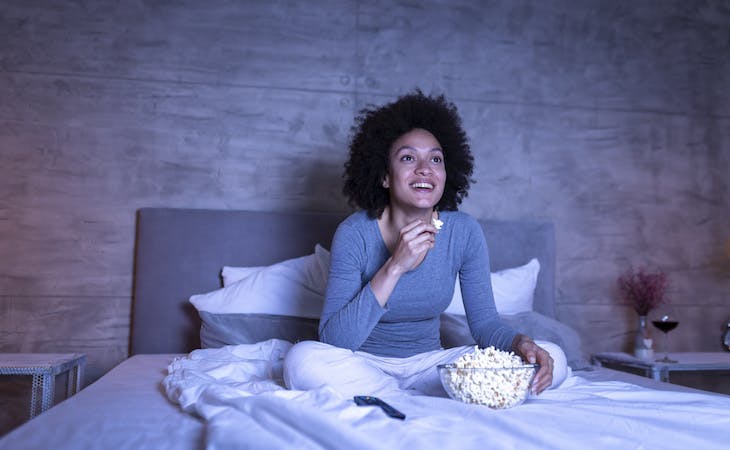 person watching tv in bed with popcorn