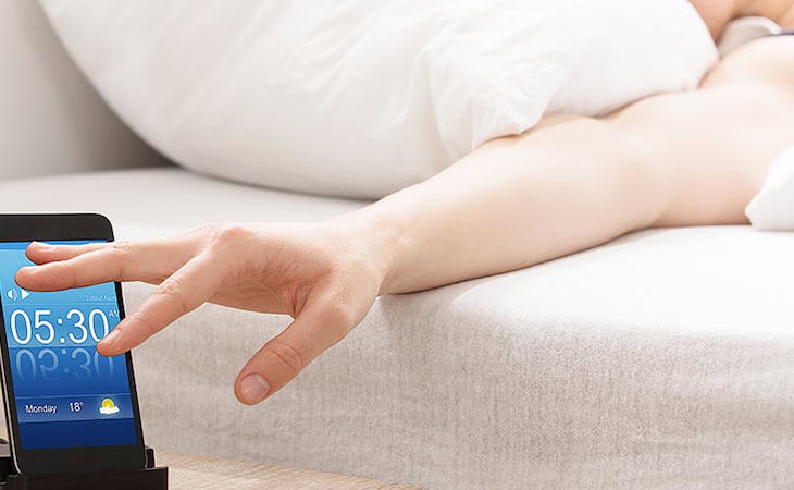 image of woman reaching for alarm clock in bed