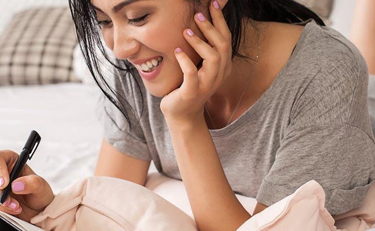 image of woman writing in journal in bed