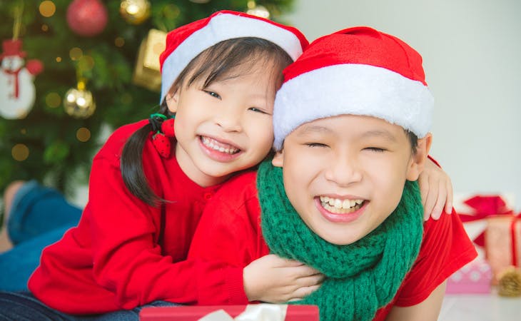 two children smiling in front of christmas tree