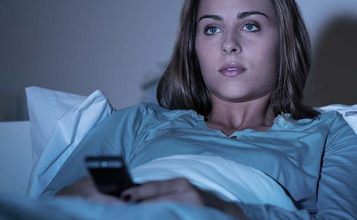 image of woman binge-watching tv from bed