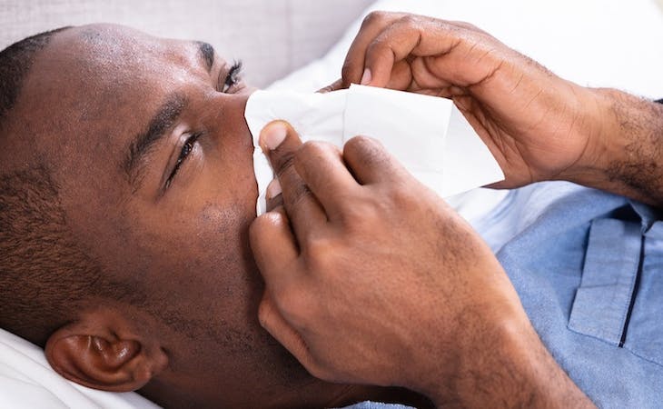 image of person with allergies blowing nose in bed
