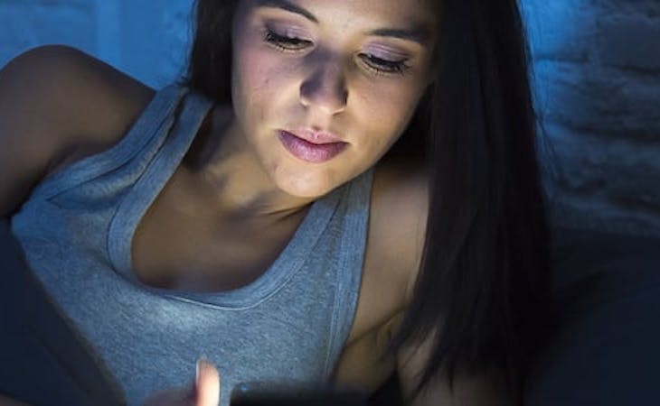 person looking at phone, which emits blue light, in bed