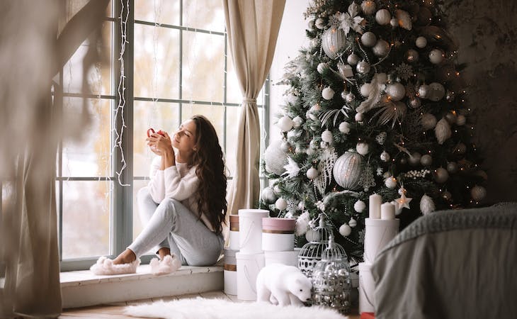 image of person in cozy loungewear sitting on windowsill in front of christmas tree