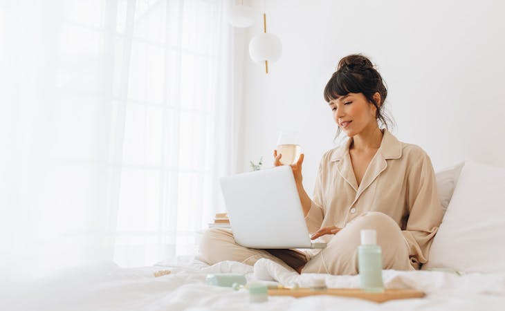 person working from home in bed drinking tea with laptop