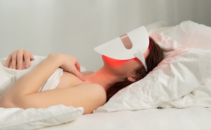 person lying in bed wearing a red light therapy face mask