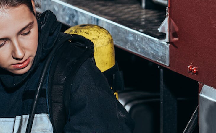 tired firefighter sitting against firetruck