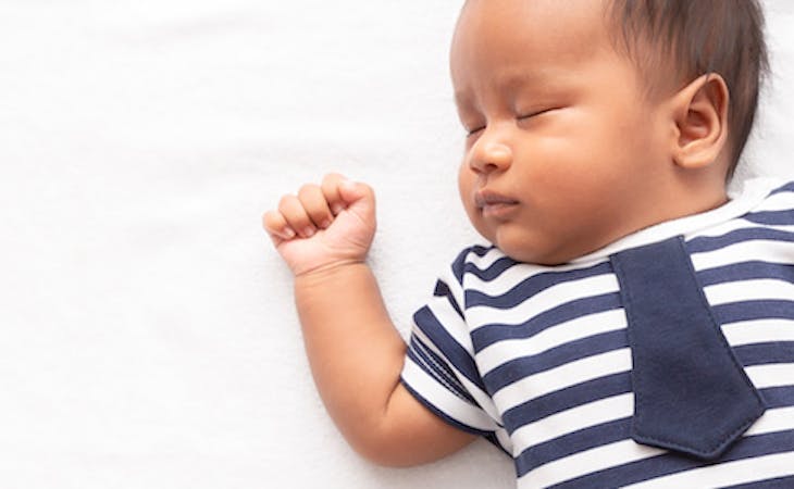 baby sleeping on top of bed with arm raised