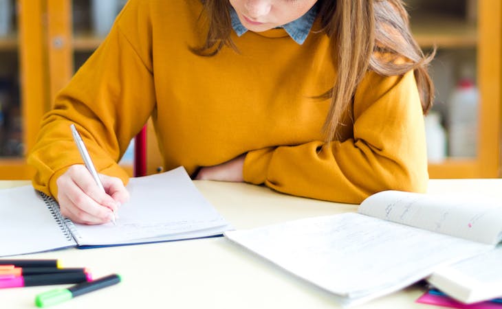 student taking notes with highlighters and textbooks on her desk