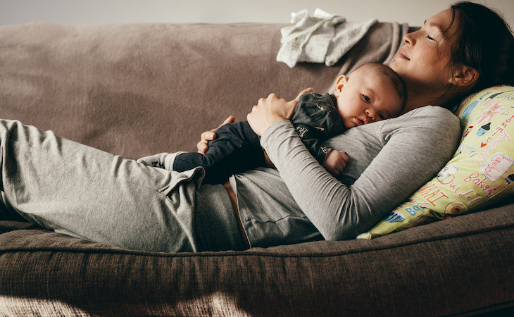 tired mom sleeping on couch holding baby