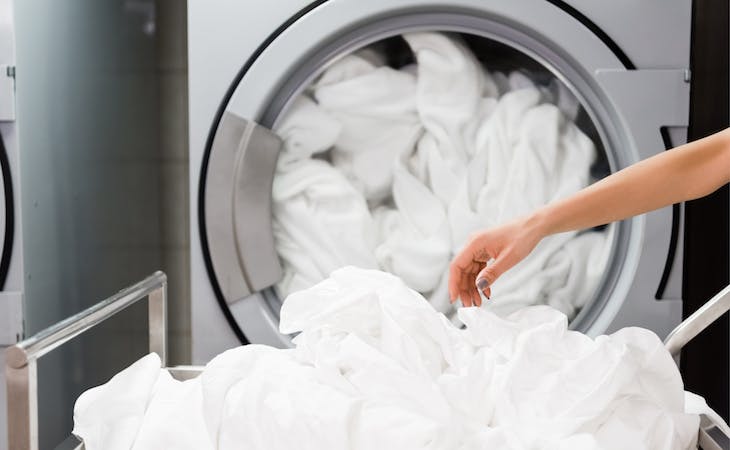 person putting sheets in washing machine to get blood out of sheets