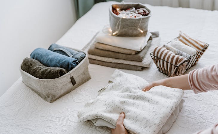 person spring cleaning with folded clothes in bins