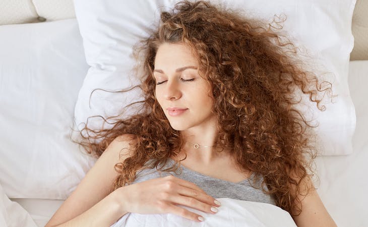 person with curly hair sleeping in bed