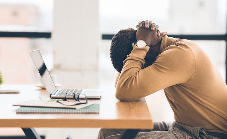person with burnout with head in hands falling asleep at desk