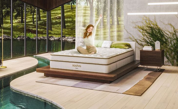 person sitting on saatva mattress in bedroom with nature all around them
