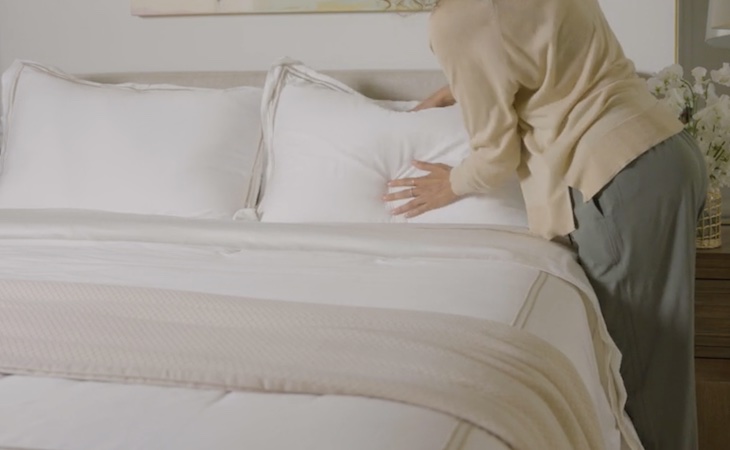 person fluffing a pillow on the bed