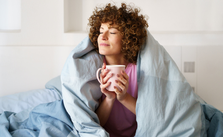 person drinking ayurvedic tea wrapped under blanket in bed