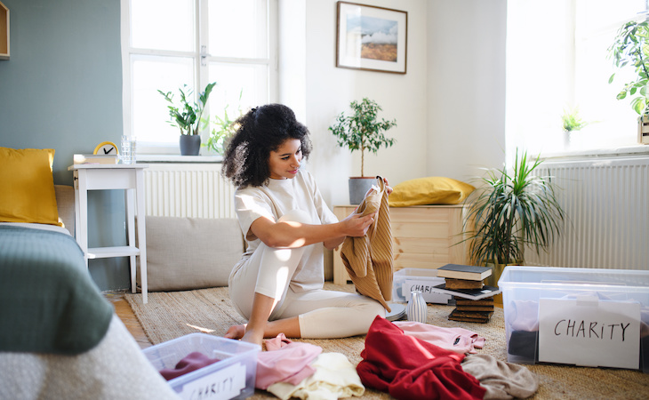 person decluttering bedroom by sorting clothing for donation