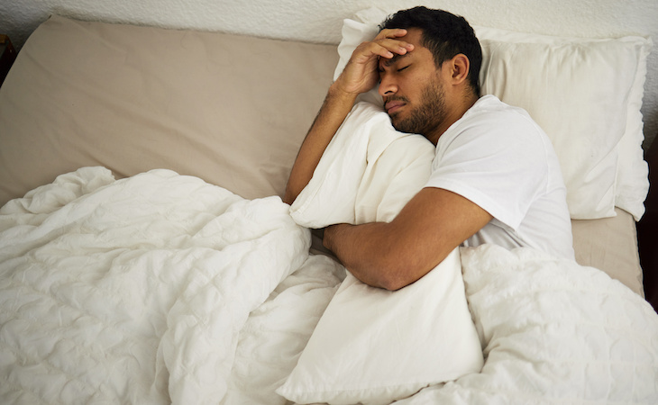 person with insomnia holding head in bed