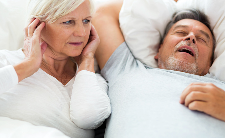 couple in bed - one person snoring and the other person is blocking ears to drown out noise