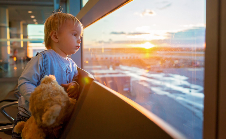 baby holding stuffed animal looking out window in airport while traveling