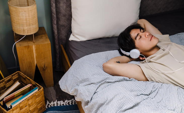 person lying in bed listening to binaural beats in headphones