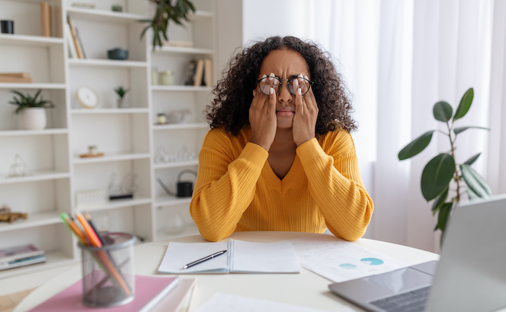 person rubbing irritated eyes, sitting at desk