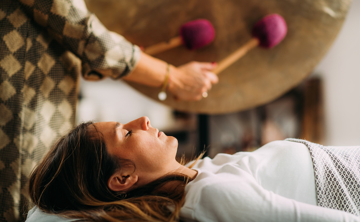 person lying down while another person plays going in sound bath therapy