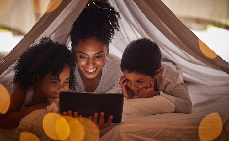 parent putting kids to sleep reading on tablet