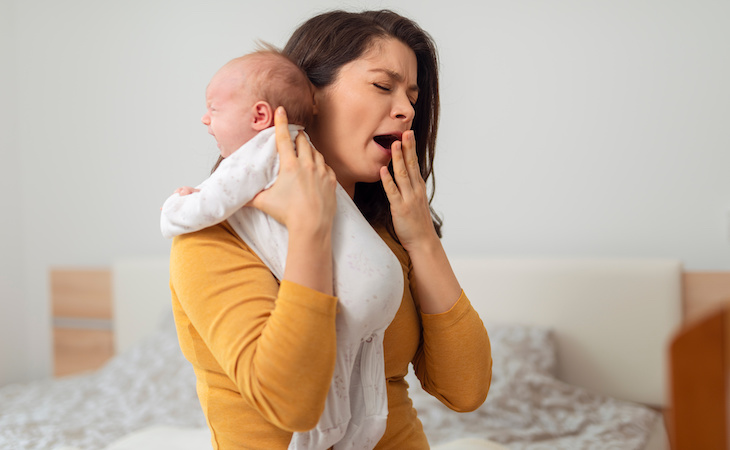 tired mom yawning while holding baby