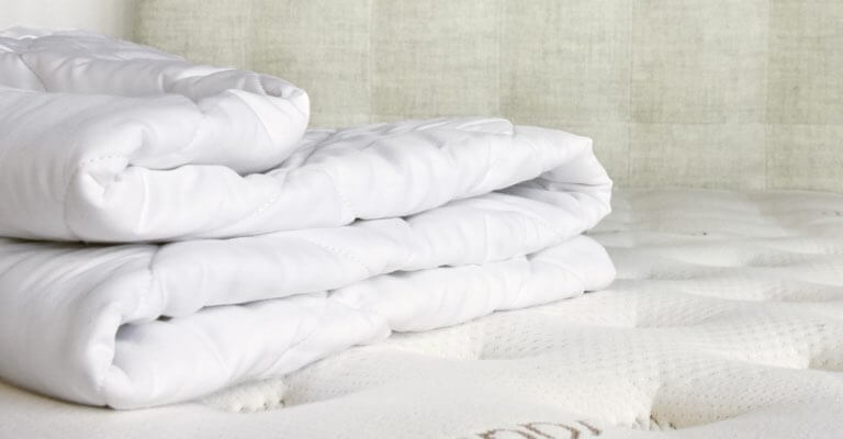 A Saatva mattress pad folded up on a Saatva mattress.