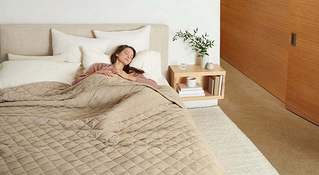 Woman laying on bed covered in a weighted blanket.