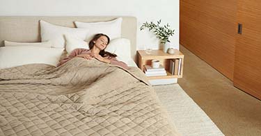 Woman laying on bed covered in a weighted blanket.