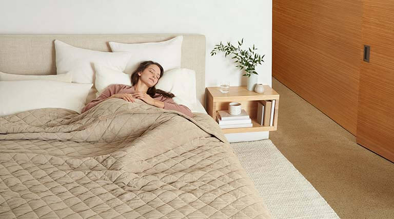 Woman laying on bed covered in a weighted blanket.
